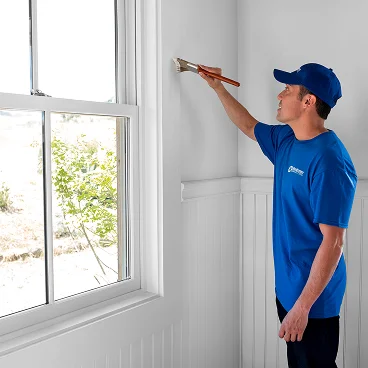 Professional painter applying paint near a window inside a bright interior room.