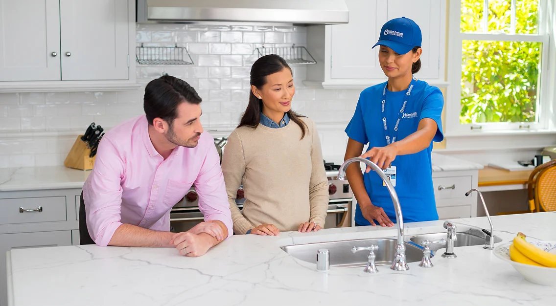 Homeowners reviewing a kitchen sink installation with a professional plumber in a modern white kitchen.